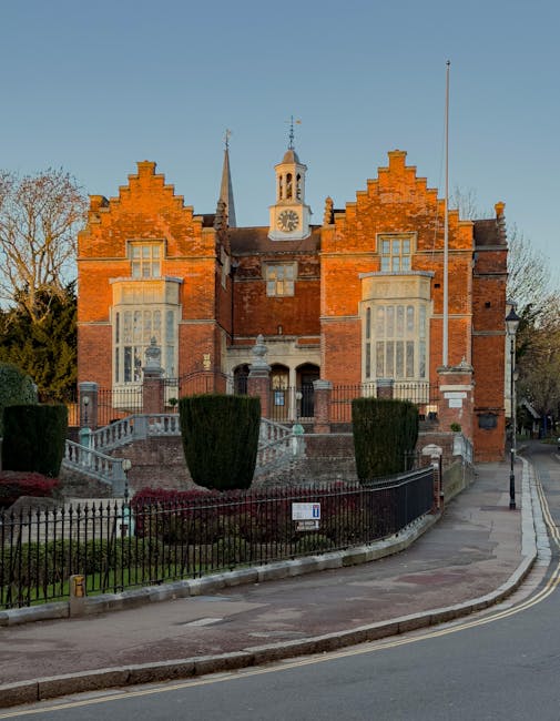 The image showcases a row of vibrant, fresh bouquet arrangements placed on a white table outside, in front of a historic red-brick building with ornate architectural details, small towers, and a centr