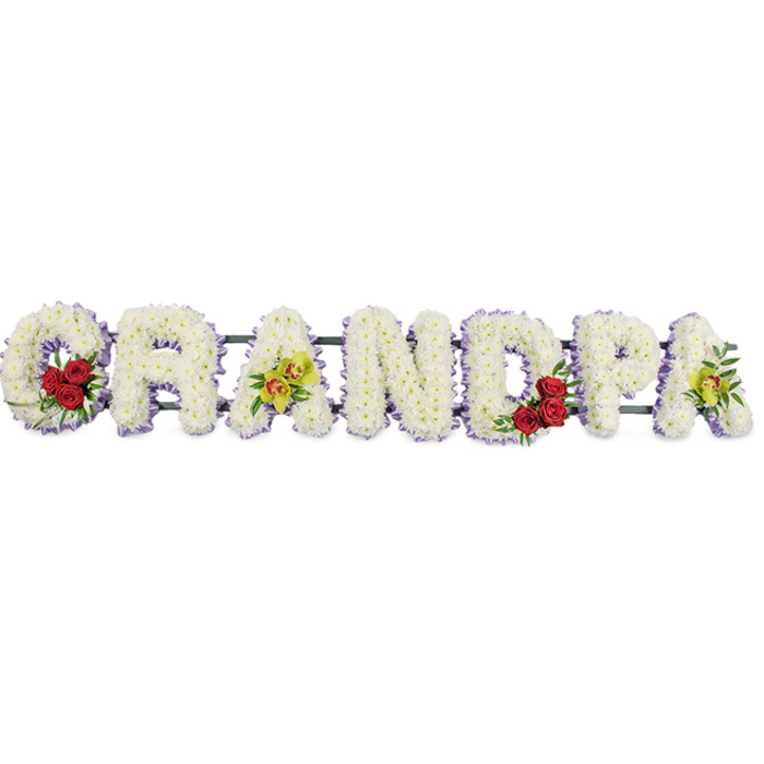 A large, handcrafted floral tribute spells out "GRANDPA" in capital letters, displayed in a straight line against a crisp, white background where nothing distracts from the flowers. Each letter is built up with a dense covering of white chrysanthemums, the small blossoms placed so closely together that they form a seamless, pillowed surface. The petals create a soft, velvety texture that visually softens the strong letter shapes, making the tribute feel kind, tender, and deeply respectful. Tracing the outer edge of every letter, a neat band of light purple ribbon forms a continuous outline, like a delicate frame that gently defines the design and adds the faintest suggestion of colour, similar to the soft evening tones often seen over nearby parks and streets in Wealdstone. To bring depth and individuality to the piece, the florist has added contrasting floral clusters. In the curve of the "G" and the rounded interior of the "D," small groups of three or four deep red roses nestle among the white blooms, surrounded by lush green foliage. Their rich, ruby colour and velvety petals form striking focal points, symbolising deep love, devotion, and treasured memories. On the first "A" and the last "A," yellow-green orchids with hints of red or brown patterning are arranged with care, their exotic shapes and fresh tones suggesting admiration and lasting remembrance. Narrow metal or wooden supports underneath link the letters together discreetly, keeping the word straight and secure for display at a funeral service, memorial, or graveside. Created in the thoughtful style of an experienced Wealdstone florist, this "GRANDPA" tribute balances purity, colour, and texture to honour a much-loved grandfather with quiet grace.