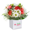 There's an inviting, lighthearted energy to this bouquet-its colours, forms, and textures reminiscent of a breezy day among Wealdstone's tree-lined avenues. Coral and rich red carnations, soft and densely frilled, form the arrangement's spirited core, while bright white daisies with luminous yellow-green eyes punctuate the bouquet, adding a burst of sunny charm. Threads of delicate gypsophila drift between petals, giving an impression of airy weightlessness that feels both innocent and uplifting-like the first days of spring at Harrow Recreation Ground. Glossy, shade-deep leaves wrap the flowers at their base, their broad, elegant shapes catching the light and framing the display with vibrancy. Emerging from amongst the blooms are a few slender buds tinged with purple, hinting at freshness and the promise of new blossoms yet to unfold. Crafted into a generous, rounded form and complemented by a pristine square gift bag with sturdy ribbon handles, the bouquet is as pleasing to the eye as it is heartfelt in its intent. Whether gifted for a birthday, shared in celebration, or offered simply to brighten another's day, this arrangement embodies the joy and stewardship of experienced local florists, ready for thoughtful delivery throughout Wealdstone.